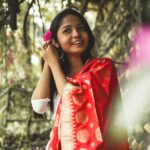 A young woman in a red saree smiling amidst nature, embodying vibrant Indian culture.
